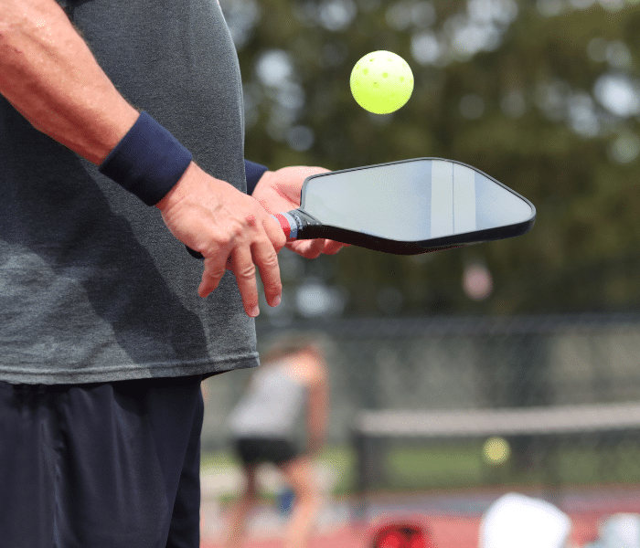 Man holding pickleball racket with ball on the court